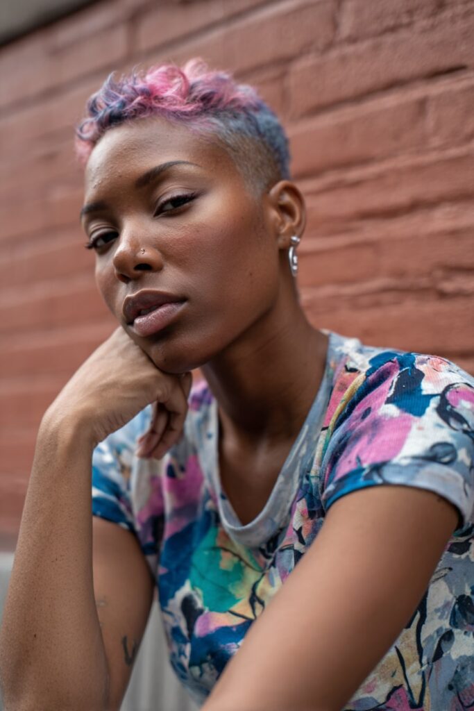 Spiky pixie cut with vibrant dyed tips in bold hues of pink, purple, and blue, worn by a confident model in funky attire in front of an urban background.