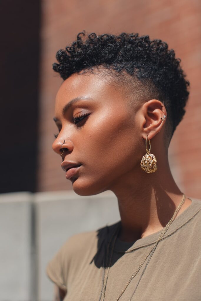 Bold Black model with a curly pixie cut and clean shaved sides, styled with top coils and gold hoop earrings, Jayda Wayda-style.