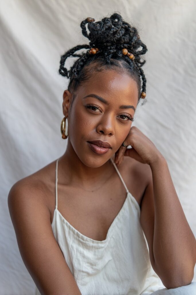Close view of Jayda Wayda-style knotless braids detailed with gold and wood beads, curly ends, and styled baby hairs, captured against a white seamless backdrop.