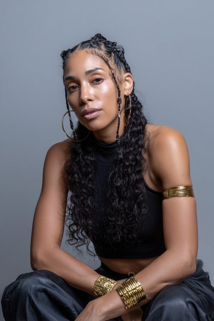 African-American woman wearing Fulani-style braids with a middle braid and curly ends, adorned with gold cuffs and styled baby hairs.