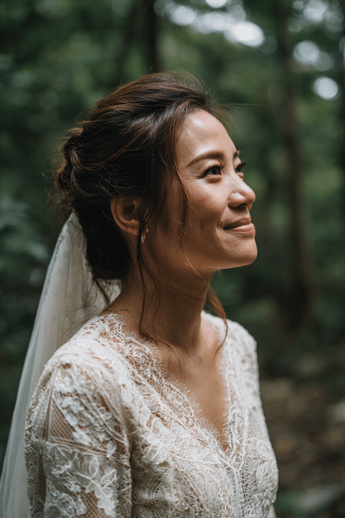 American bride with a half-up half-down hairstyle flowing into a long veil, wearing a modest lace bridal gown in a lush forest backdrop.