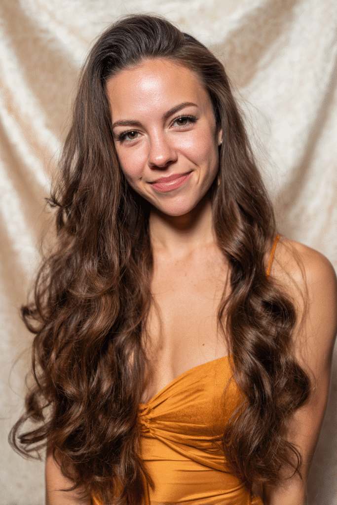 A vibrant female model in her 20s with shoulder-to-waist-length wavy half wig, styled with loose waves flowing down, photographed against a seamless light beige backdrop with a glossy sheen. She wears subtle makeup, a trendy outfit, and has a warm skin tone with a friendly expression, captured with soft natural lighting.