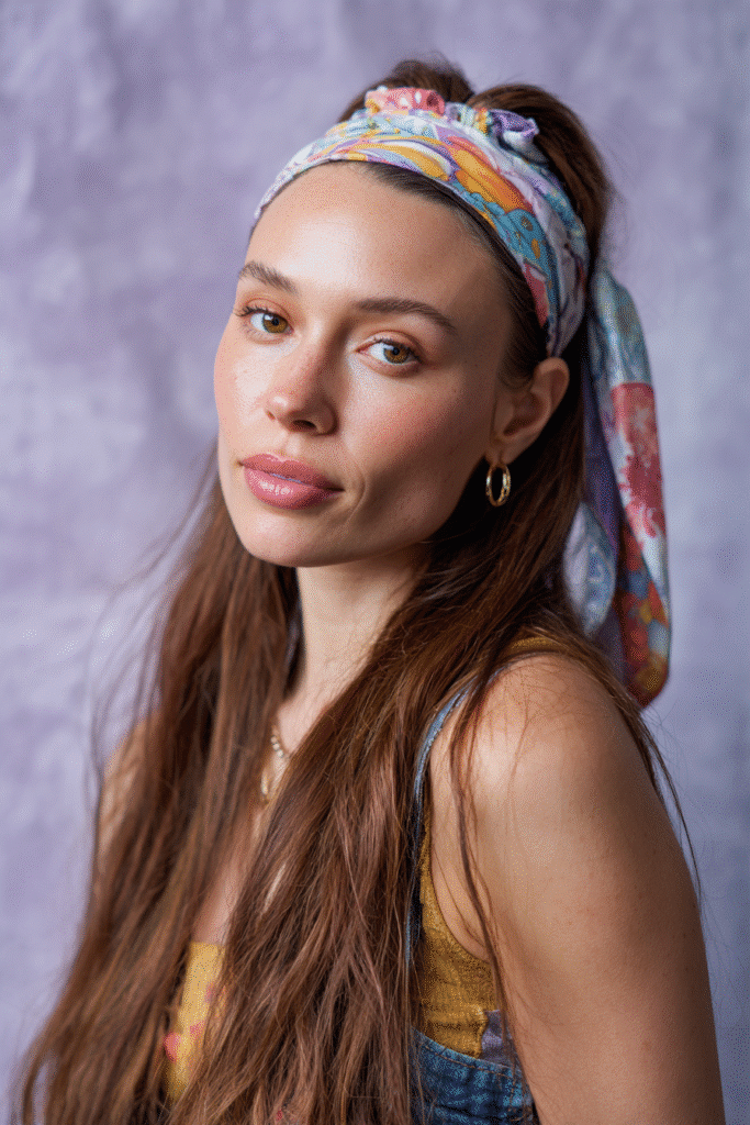 A vibrant female model in her 20s with shoulder-to-waist-length straight half wig, styled with a colorful fabric headband and loose strands flowing down, photographed against a seamless soft lavender backdrop with a silky finish. She wears subtle makeup, a trendy outfit featuring a tailored blazer, high-waisted jeans, and stylish ankle boots, accessorized with statement earrings and a chic handbag, with a warm skin tone and friendly expression, captured with soft natural lighting.