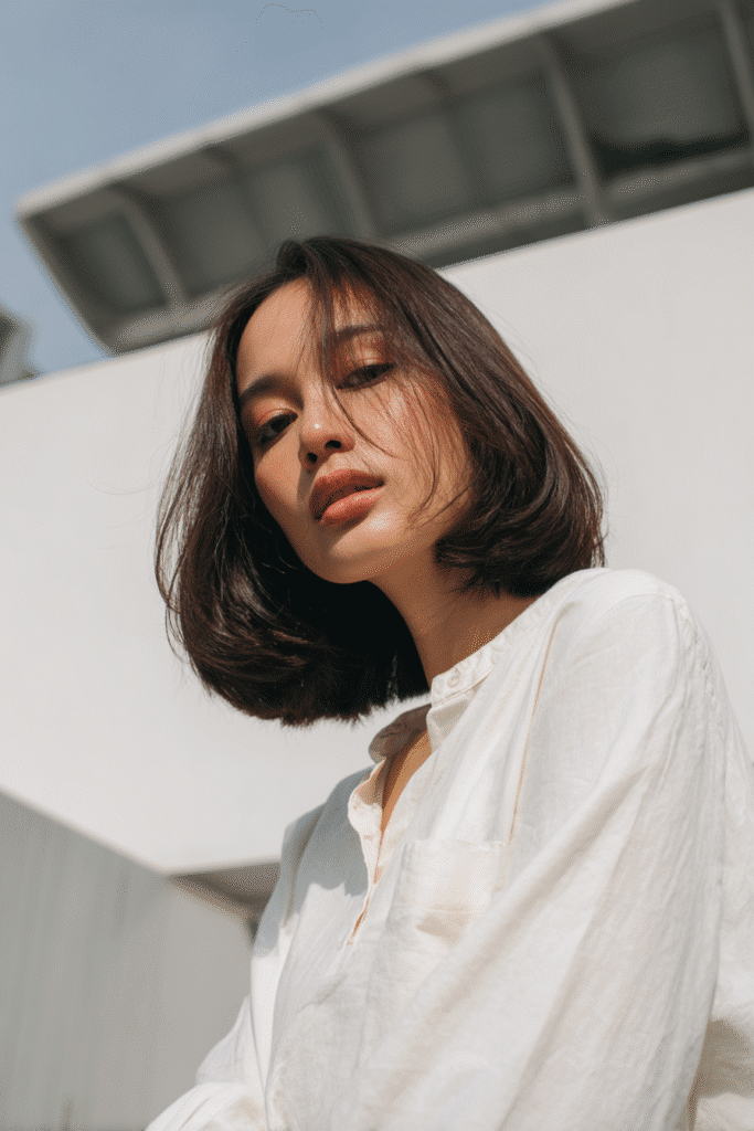 American woman with thin hair styled in a neck-length French bob, wearing a modest long-sleeve blouse, photographed against a seamless white backdrop.