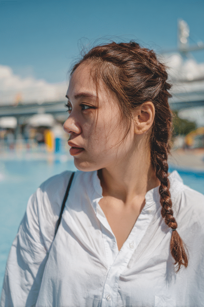 American girl with curly hair styled in a pineapple updo, wearing a full swim shirt, standing in a vibrant splash zone.