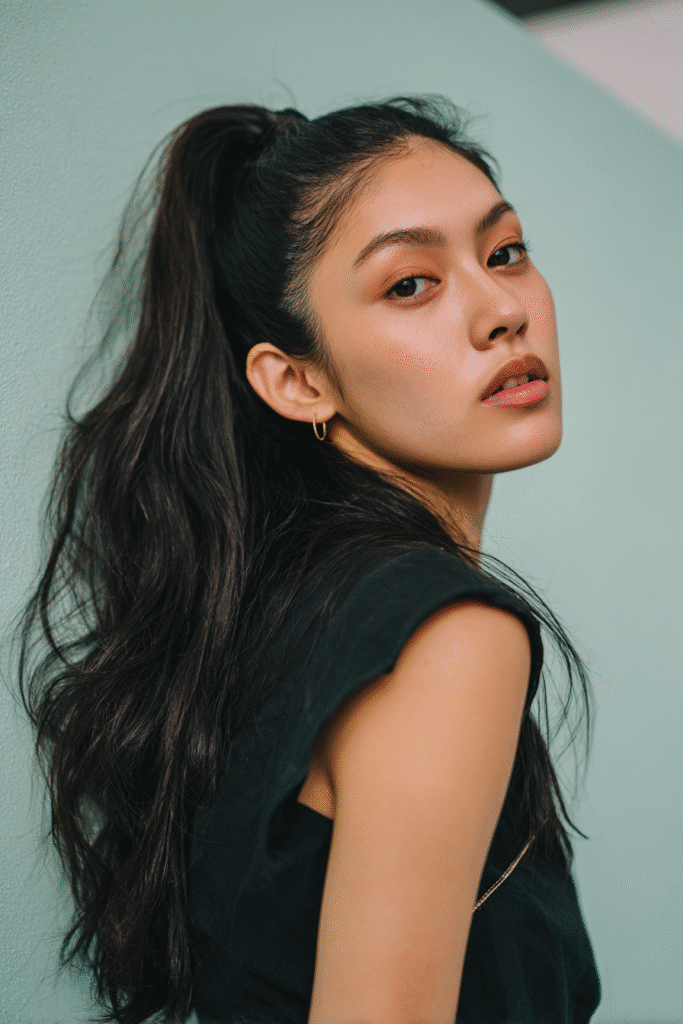 A stunning young woman in her 20s with natural skin tone, showcasing a homecoming hairstyle with a high ponytail, featuring a smooth, voluminous ponytail, captured in a close-up shot focusing on the hair, photographed against a seamless soft mint backdrop with a silky texture. She has subtle makeup, a chic homecoming dress, realistic hair texture, warm skin tone, and a confident expression, captured with soft natural lighting and an Instagram-style beauty vibe.