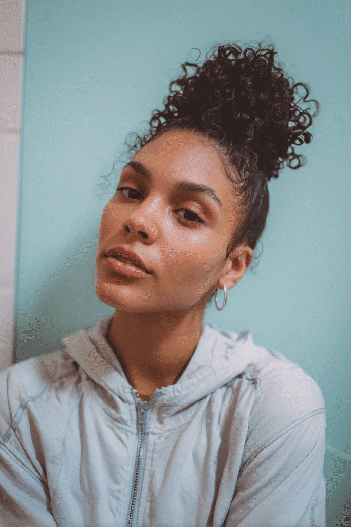 A vibrant young woman in her 20s with natural skin tone, showcasing a curly hairstyle for short hair with pinned up crown curls, featuring curls pinned into a crown shape, captured in a close-up shot focusing on the hair, photographed against a seamless light aqua backdrop with a smooth texture. She has subtle makeup, a trendy full-sleeve outfit, realistic hair texture, warm skin tone, and a confident expression, captured with soft natural lighting and an Instagram-style beauty vibe.