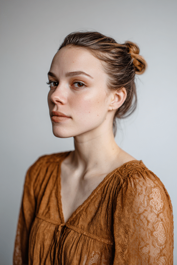 A gorgeous young woman with a natural look showcasing a sleek bun with a polished hair treatment finish in a warm golden shade, wearing an elegant full-length dress with lace long sleeves, radiant expression, warm skin tone, against a seamless soft linen backdrop with a matte finish.