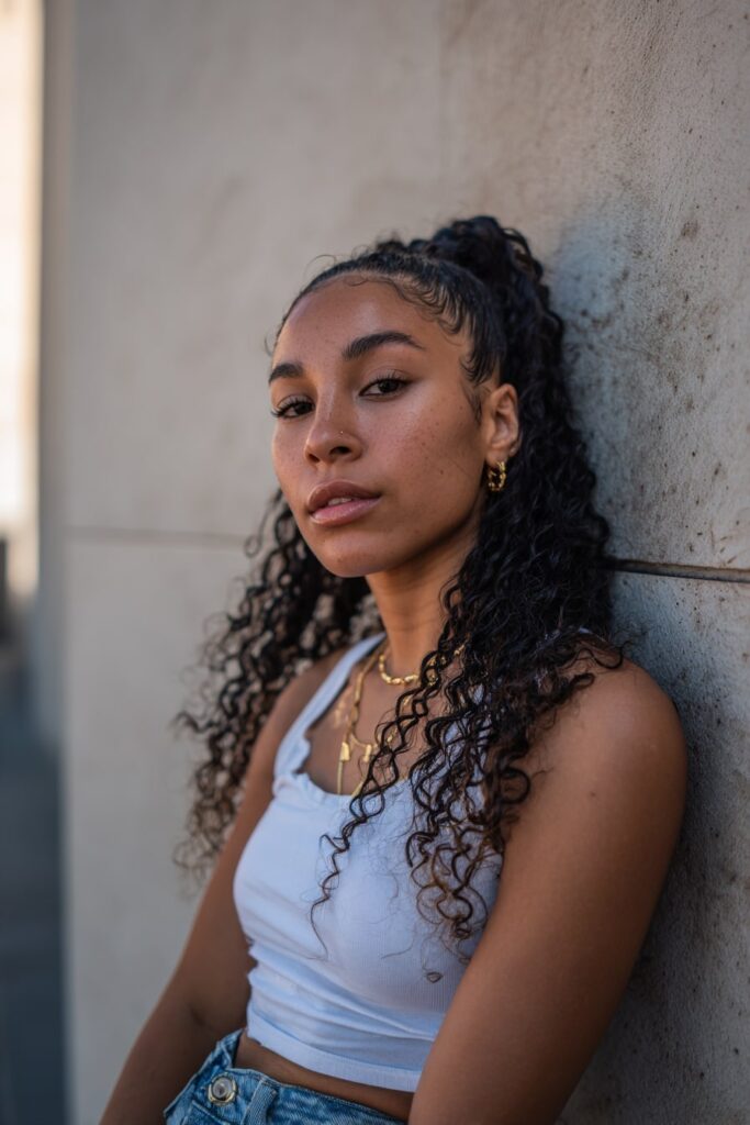 Black girl with half-up balayage curls, clip-ins, ombre hair, plaster backdrop.