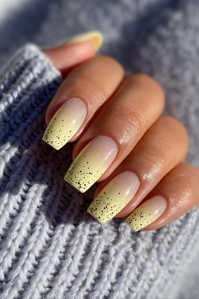 Ombre nails fading from sheer to dark with scattered black polka dot detailing.