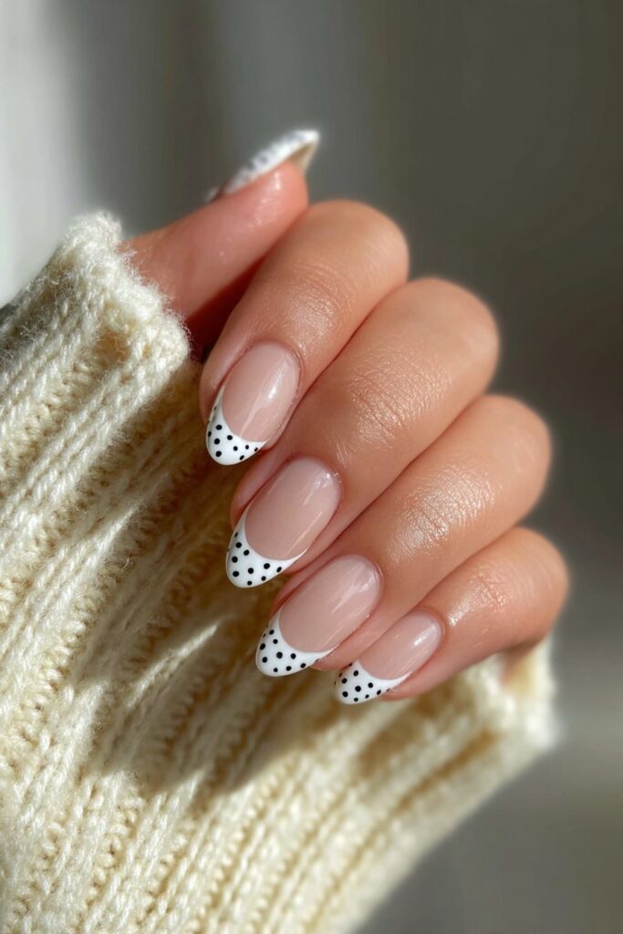 Modern French tip nails with crisp black polka dots and glossy clear base.