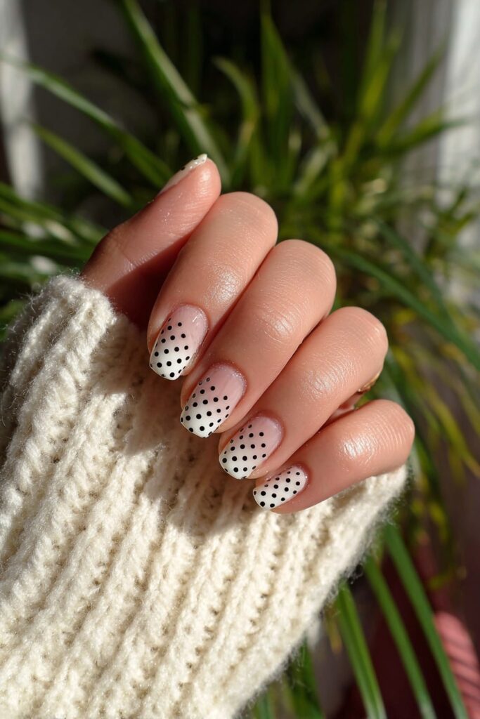 Minimalist negative space nails with black polka dots on a glossy clear base.