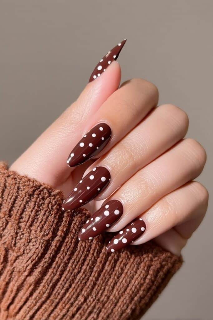 Striking reflective brown chrome nails layered with subtle white dot overlays, high-shine metallic finish with a futuristic, editorial-inspired look.