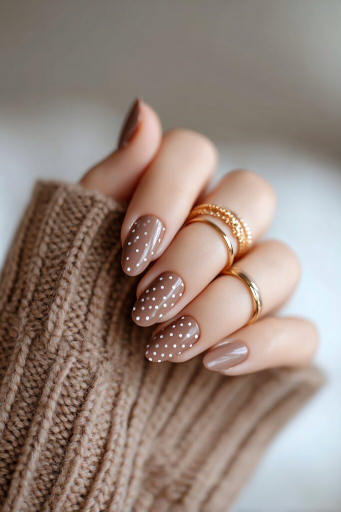 Elegant close-up of influencer’s hand featuring chocolate brown nails with tiny white polka dots, high-gloss shine, styled with a cozy brown sleeve for a chic minimalist look.