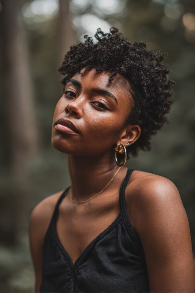 Woman with short 3c curly faux hawk, natural black hair, forest scene backdrop.