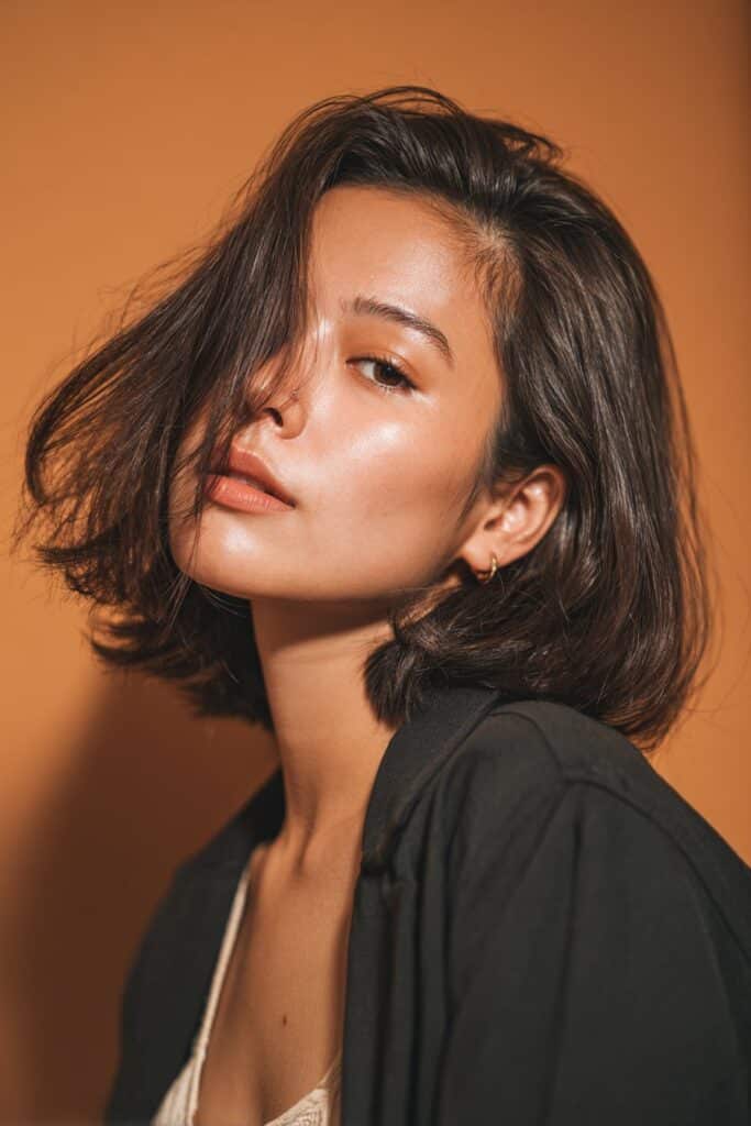A stunning young woman in her 20s with natural skin tone, showcasing a bob hairstyle for going out featuring a disconnected bob, featuring a disconnected bob with distinct layers, captured in a close-up shot focusing on the hair, photographed against a seamless dark forest green backdrop with a silky texture for optimal color contrast. She has subtle makeup, a chic evening outfit, realistic hair texture, warm skin tone, and a confident expression, captured with soft natural lighting and an Instagram-style beauty vibe.