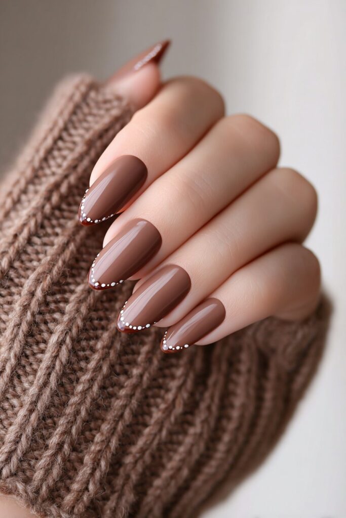 Sophisticated espresso French manicure with tiny cream dots along the tips, almond-shaped nails glowing under warm daylight, paired with a soft knitted brown sleeve.