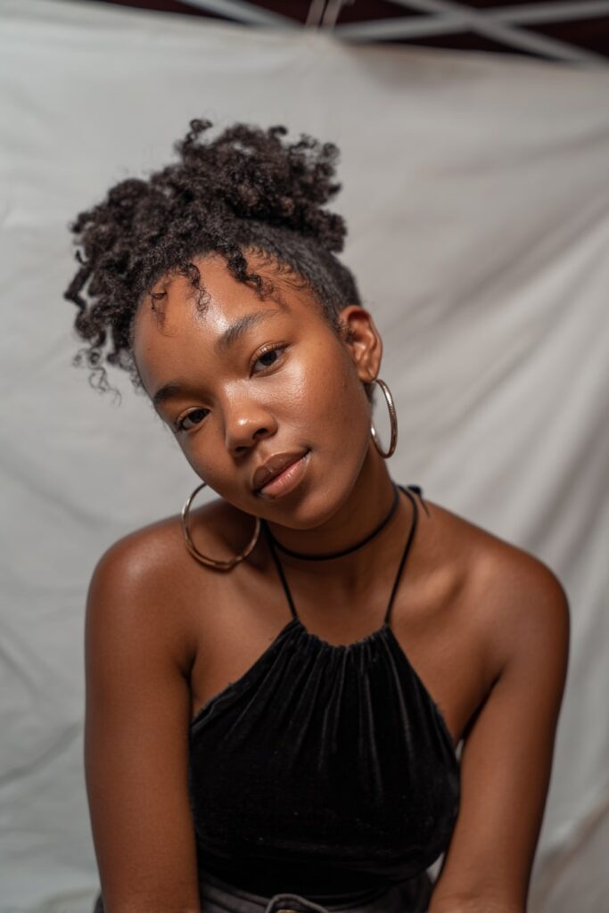 Black girl with half-up sisterlocks, curly hairstyle, natural black hair, white backdrop.