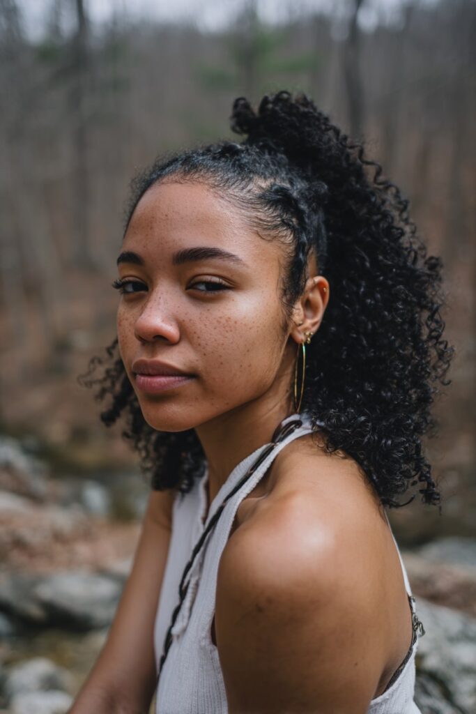Black girl with half-updo, cute curls, clip-ins, jet black hair, forest backdrop.