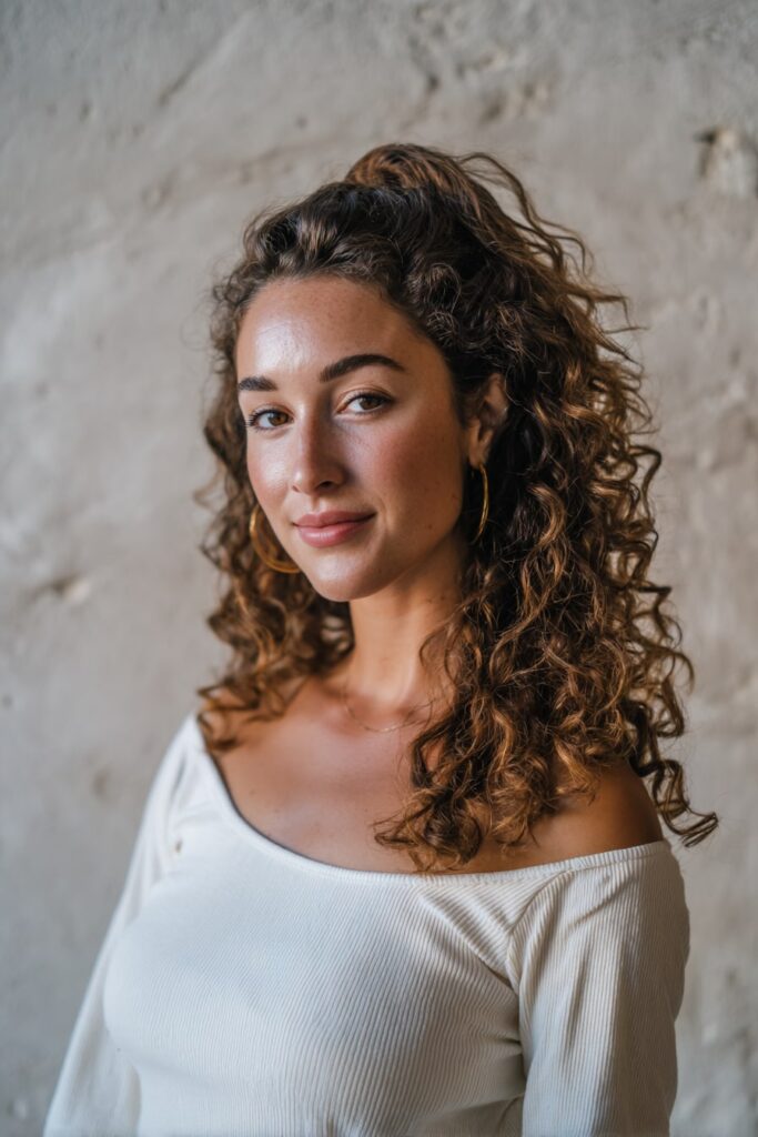 Woman with half up half down curly hair, loose twists, ombre curls, plaster backdrop.