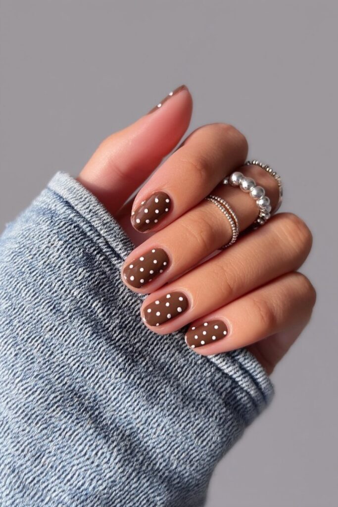 Neat short almond nails in glossy chocolate brown adorned with minimalist white dots, timeless and effortless brown nail inspiration.