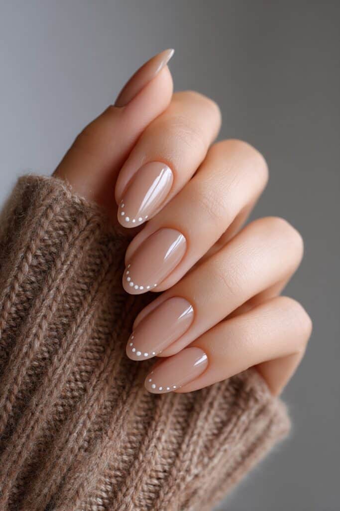 Minimal taupe French tips enhanced with delicate white micro dots on short almond nails, clean and sophisticated nail art with soft daylight tones.