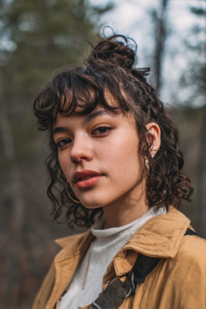 Woman with short half-up tousled curls, braided halo, natural black hair, forest backdrop.