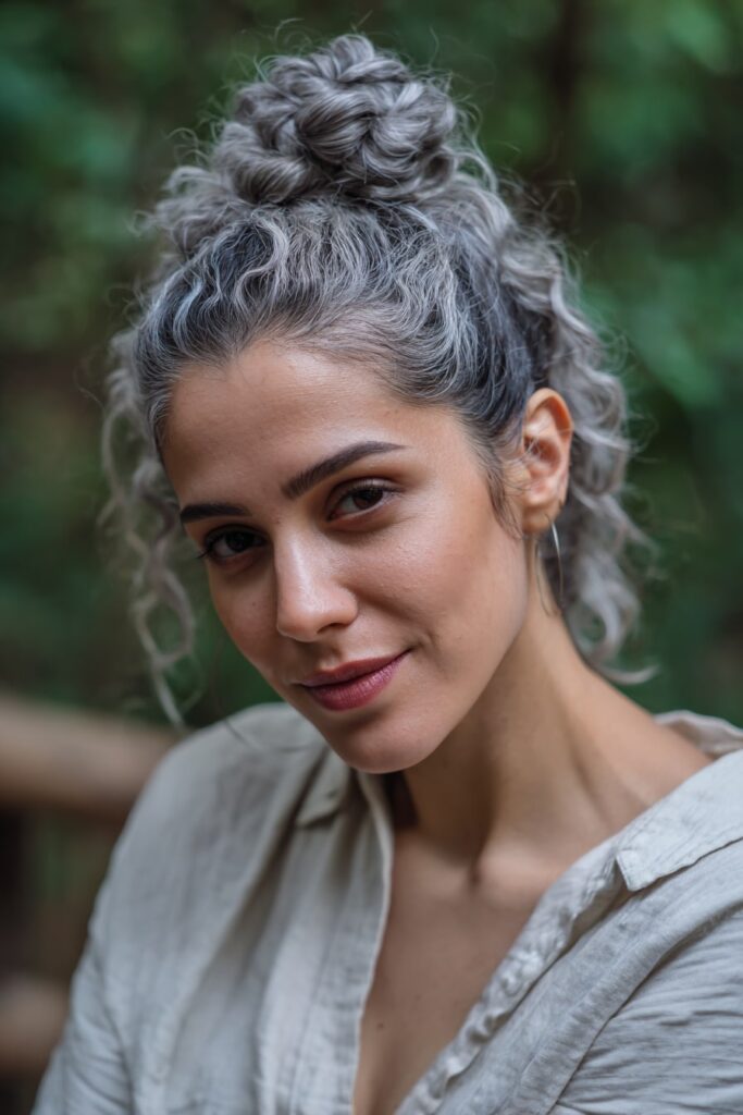 Woman with short half-up twisted knot, face-framing curls, silver highlights hair, forest backdrop.