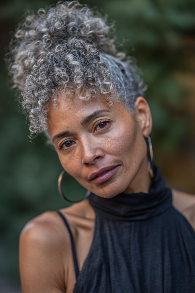 Woman with half up half down curly hair, twisted knot, face-framing curls, forest backdrop.