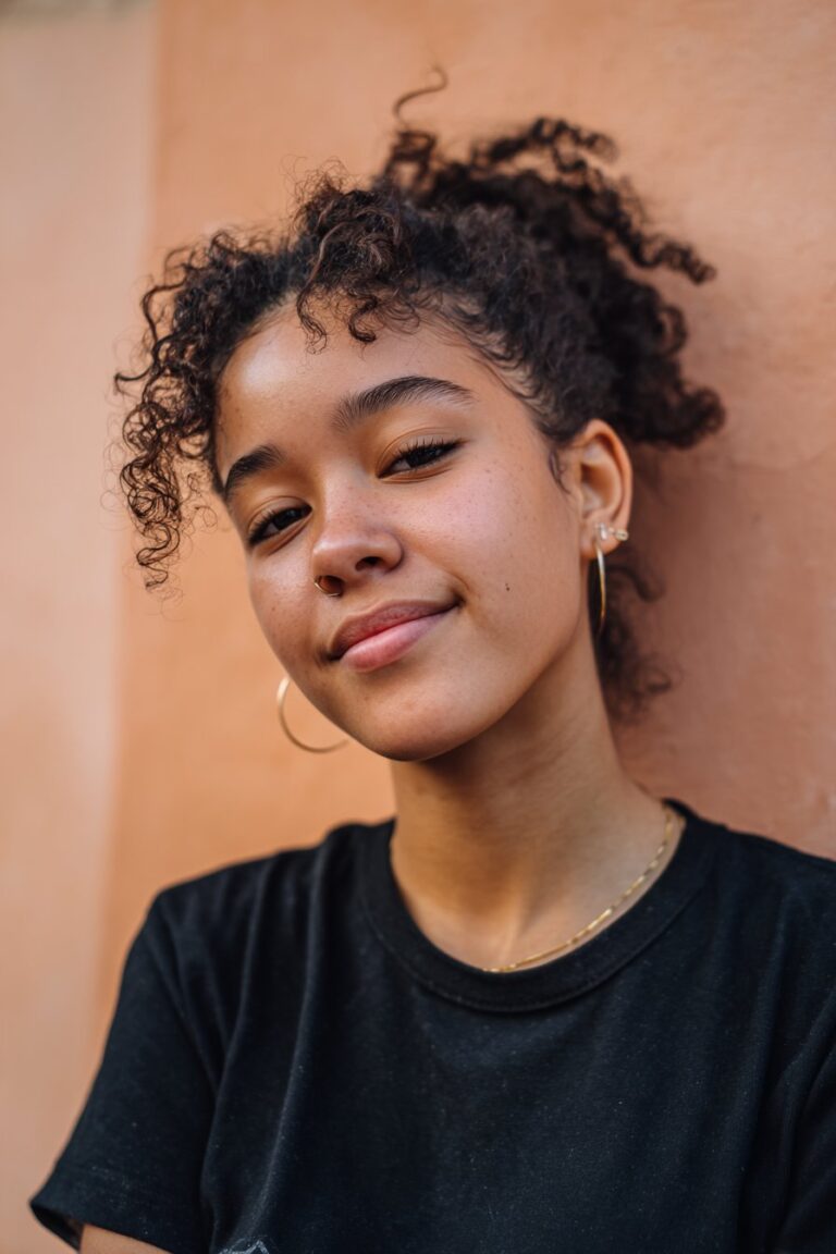 American girl with well-defined 4C finger coils, wearing a simple white long-sleeve shirt, sitting at a school desk with books, highlighting natural and defined school curls.