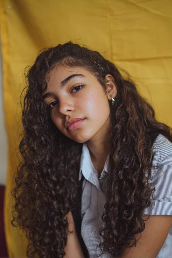 American student with short 4C hair styled in elegant finger waves, wearing a collared shirt in a classroom setting, showing a classic school hairstyle with curls.