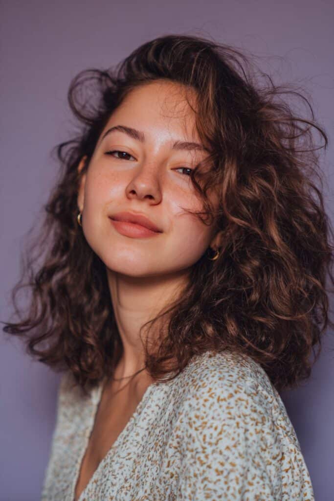 A stunning young woman in her 20s with natural skin tone, showcasing an Everyday Hairstyle For Medium Length Hair with a quick twist for shorter hair, featuring medium-length hair with a fast side twist, captured in a close-up shot focusing on the hair, photographed against a seamless warm violet backdrop with a matte finish. She has subtle makeup, a trendy outfit, realistic hair texture, warm skin tone, and a friendly expression, captured with soft natural lighting and an Instagram-style beauty vibe.
