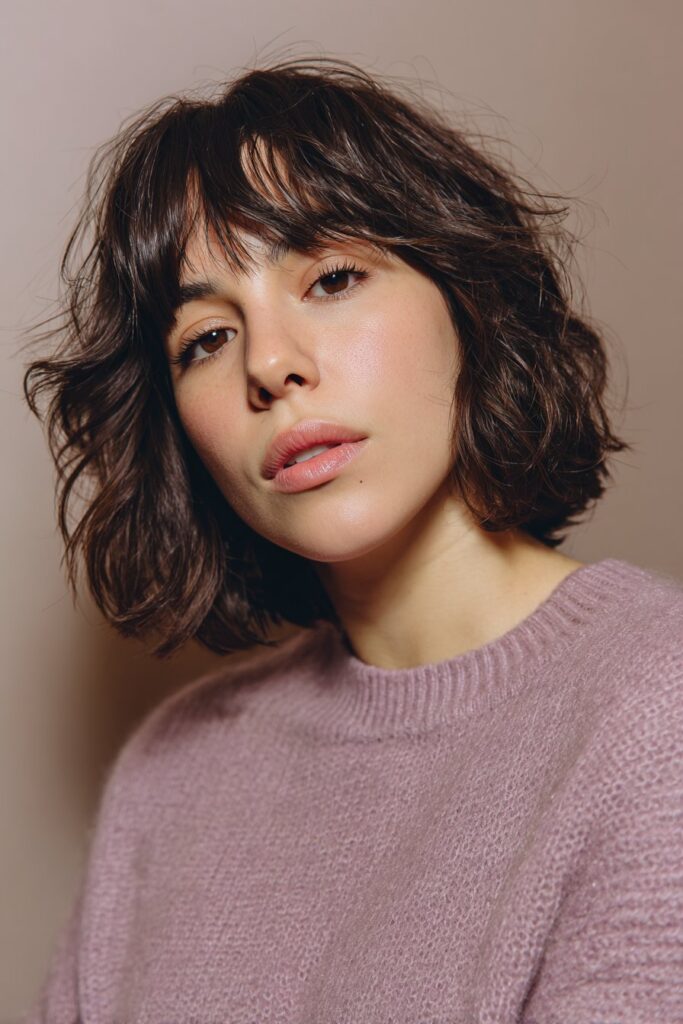 A shaggy pixie cut styled with a wispy curtain fringe and short textured layers around the face. The choppy pieces add softness and movement, creating a balanced, playful short hairstyle.