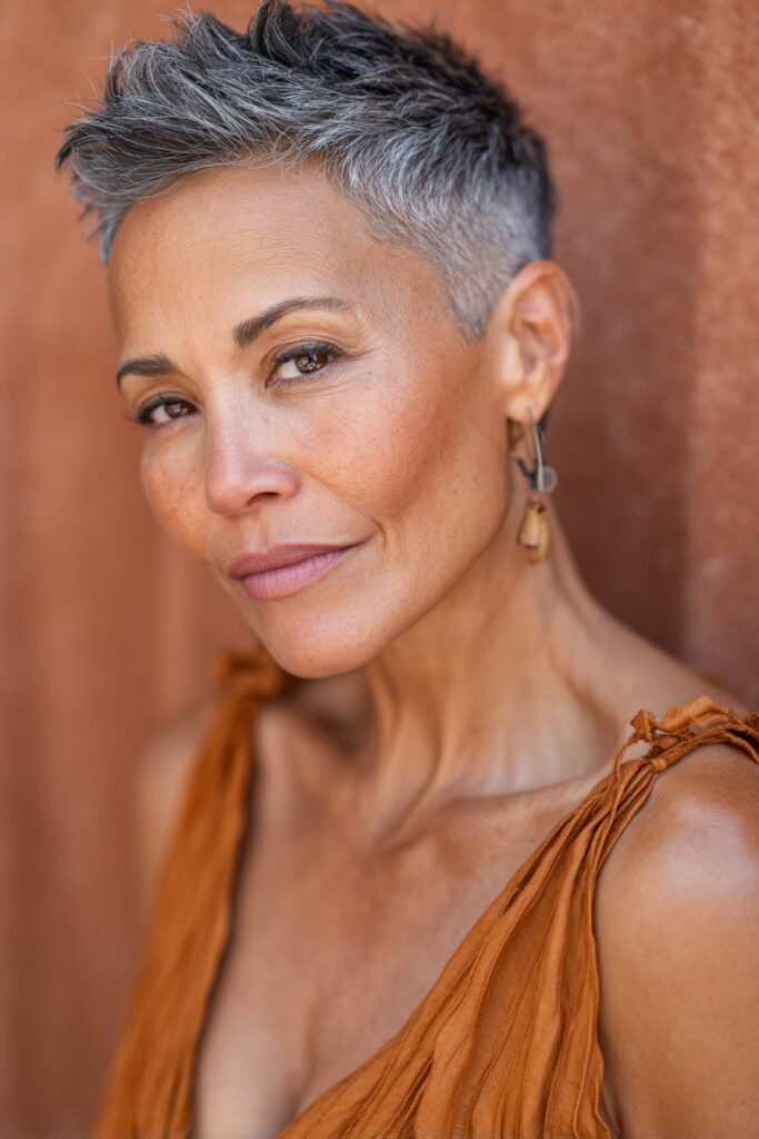 An American woman over 60 with a short tapered salt-and-pepper haircut, subtle layers enhancing her natural tones, smiling gracefully against a warm cinnamon silk backdrop.