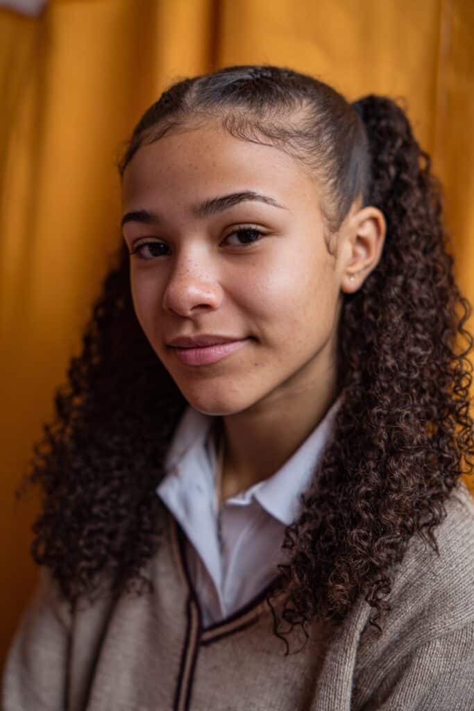 American woman with short 4C curls styled in two-strand mini twists, wearing a simple T-shirt, sitting in a study hall, showcasing a neat and protective school hairstyle.