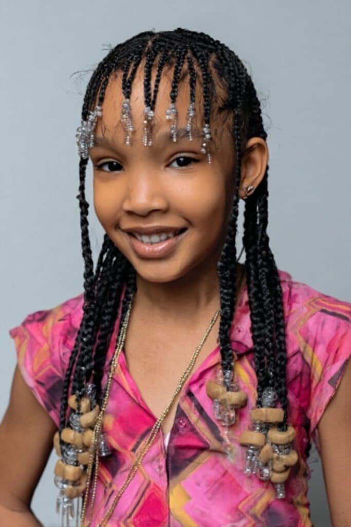 Little girl styled with neat box braids decorated with beads attached to the braids in an indoor kids studio.