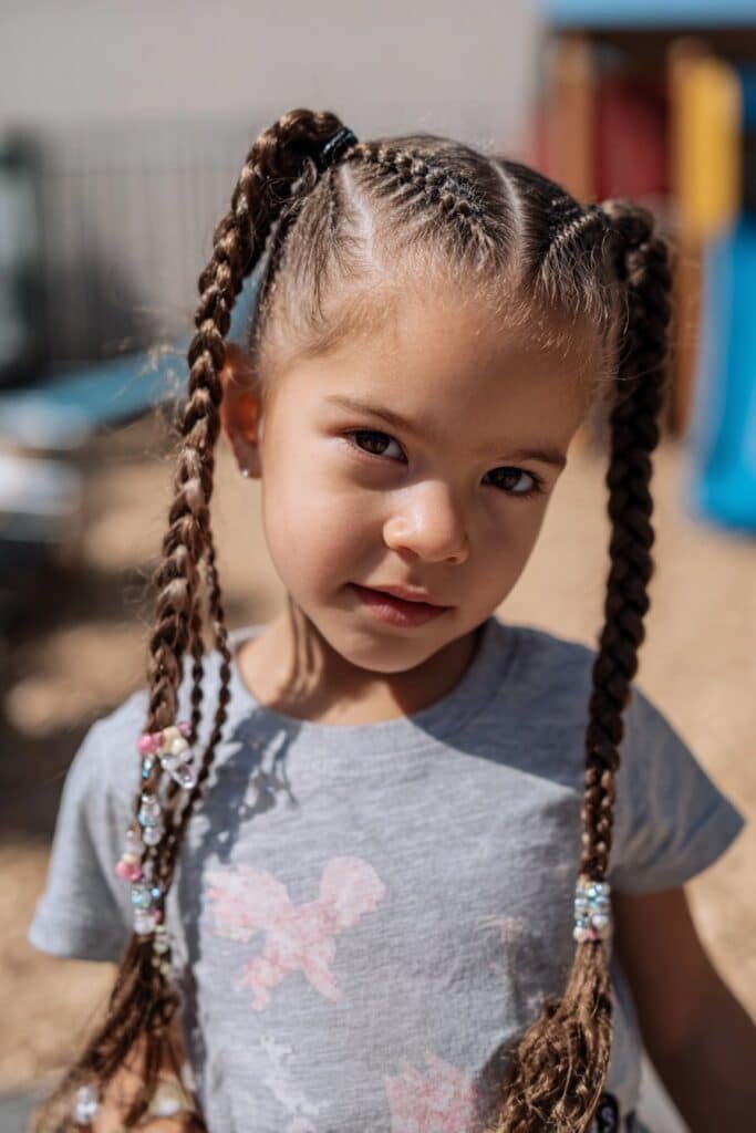 Little girl wearing braided  two sided ponytails with beads attached to each braid in an outdoor play area.