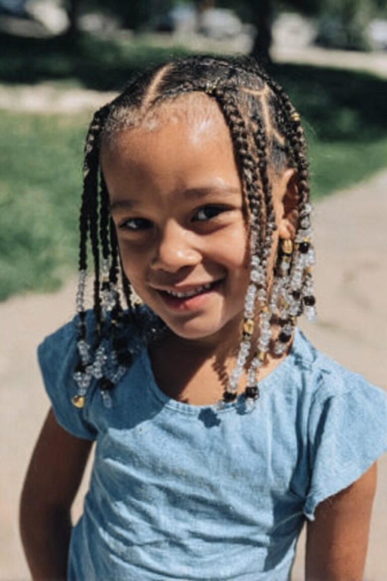 Little girl wearing braids with zigzag parting and beads attached to the braids in a park walkway.