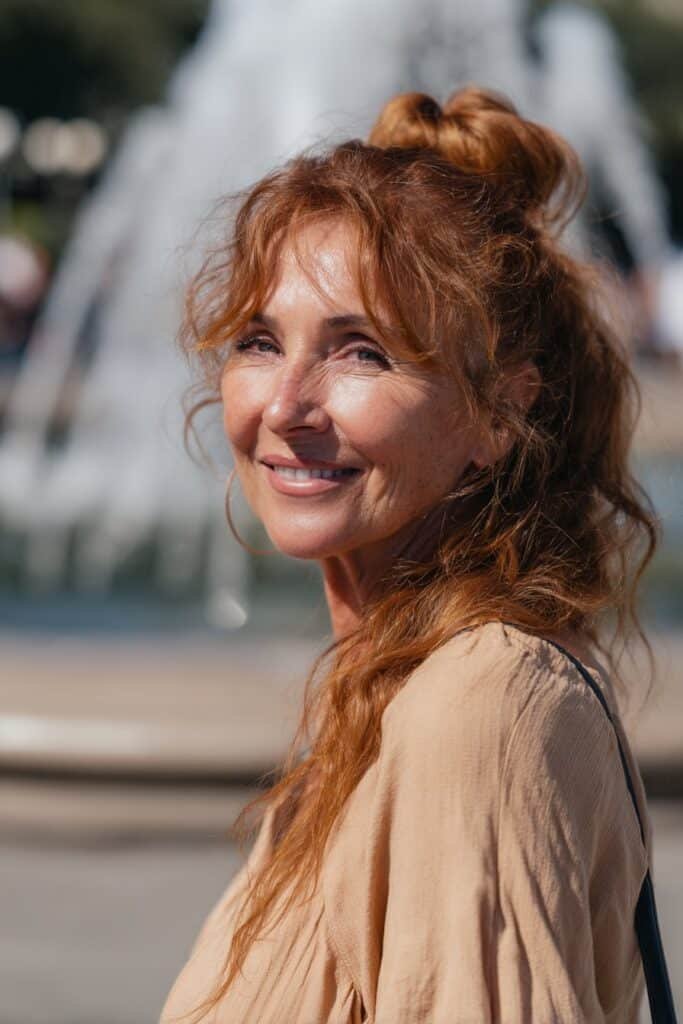 Vibrant woman in her 40s with a bubble ponytail in auburn hue, posed in a city park – ponytail hairstyles for women over 40 series.