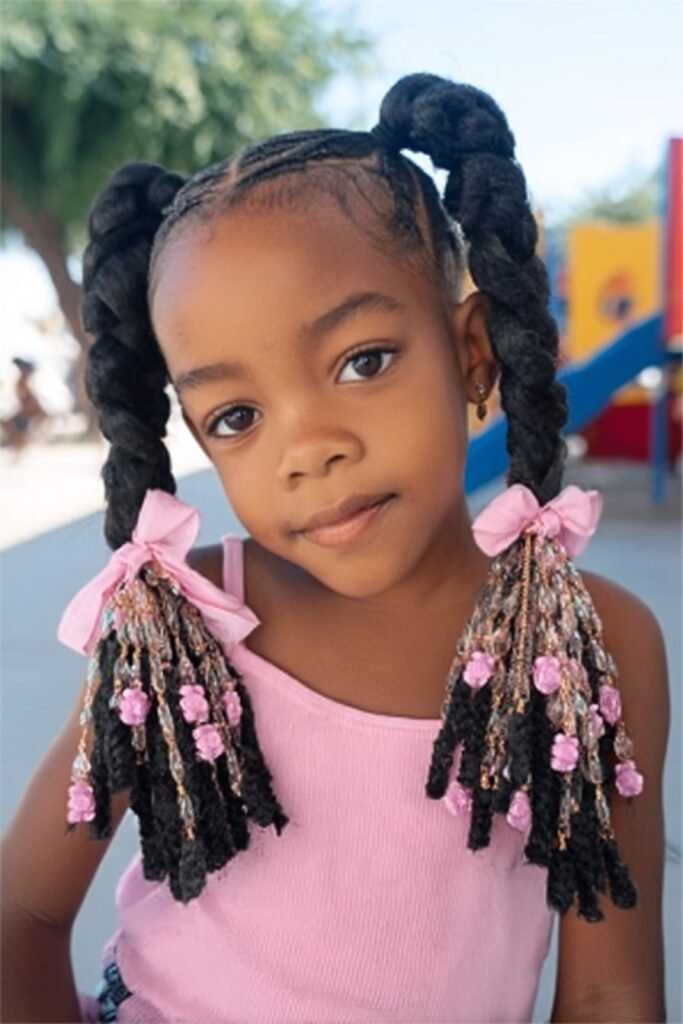 Toddler girl with double braided ponytails decorated with beads at a children’s play park.