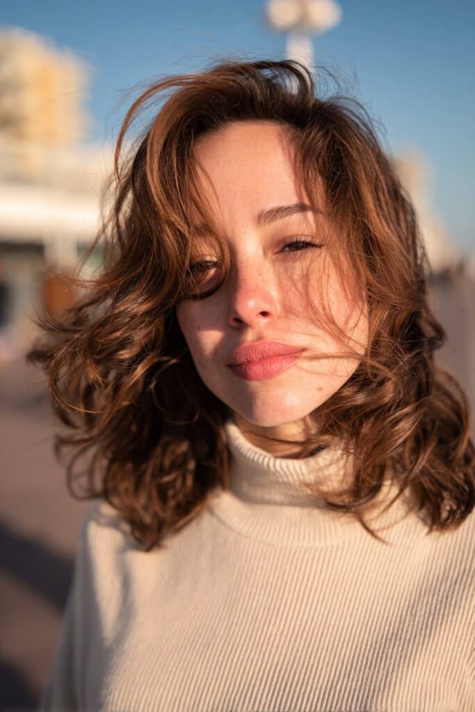 Relaxed woman wearing a light turtleneck with loose beach waves captured during golden hour at a seaside promenade.