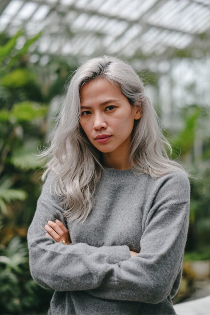 Young woman showcasing misty silver balayage, softly blended silver and icy blonde tones in a glasshouse conservatory.