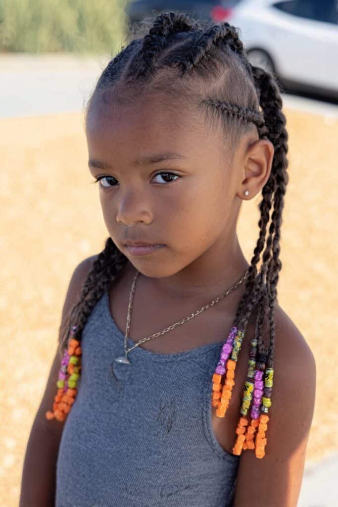 Little girl styled with mohawk braids featuring beads fixed onto the braids in an outdoor park.