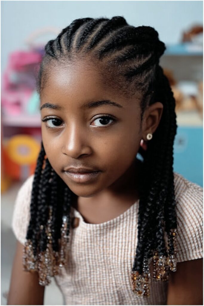 Little girl wearing simple cornrow braids with beads attached to the braid ends in a pastel playroom.