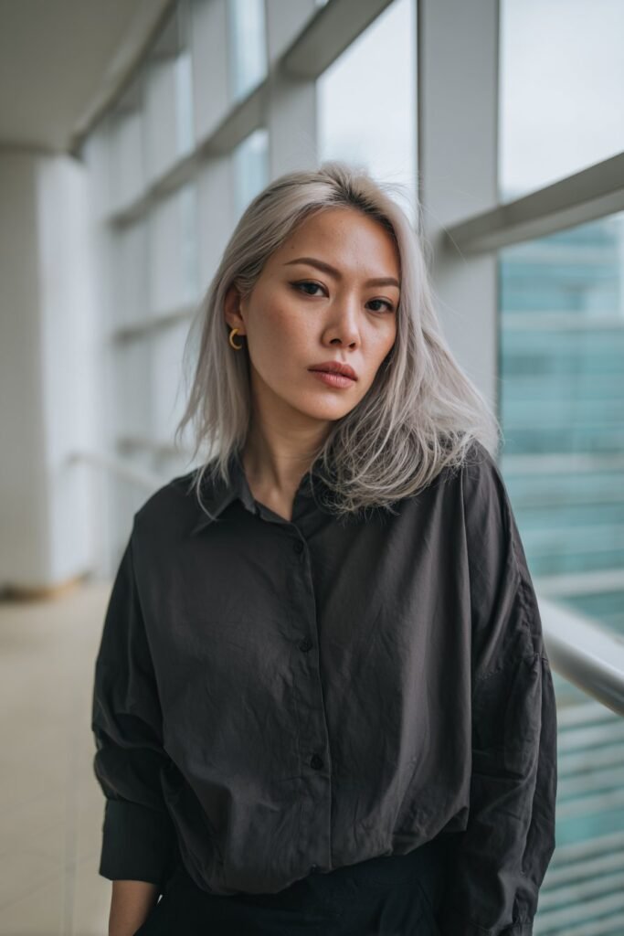 Woman in her 20s with smoky silver icy blonde hair, cool silver tones styled smoothly, photographed in a luxury penthouse interior.