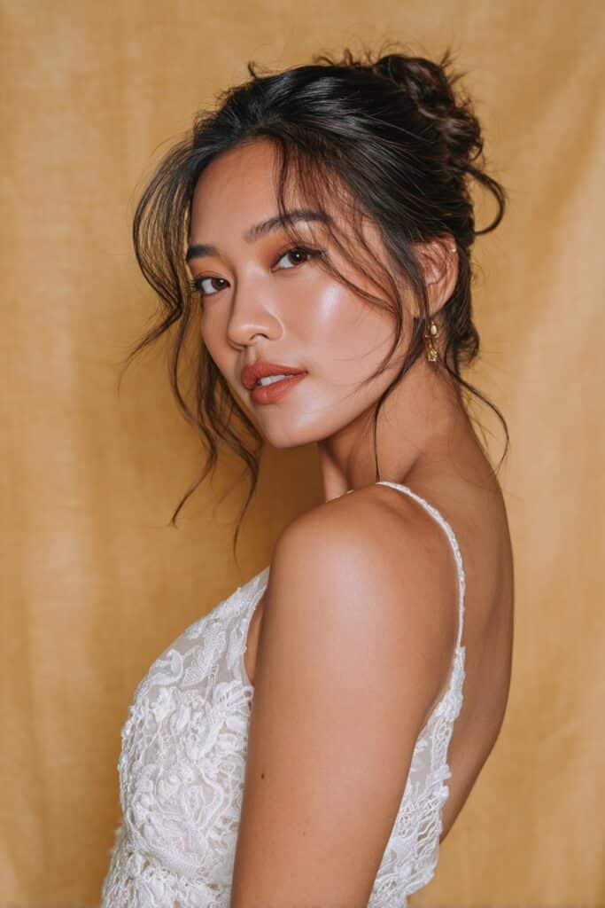 A bride with thin fine hair styled in a textured low chignon, showing soft volume and delicate detailing, photographed in bright natural light.