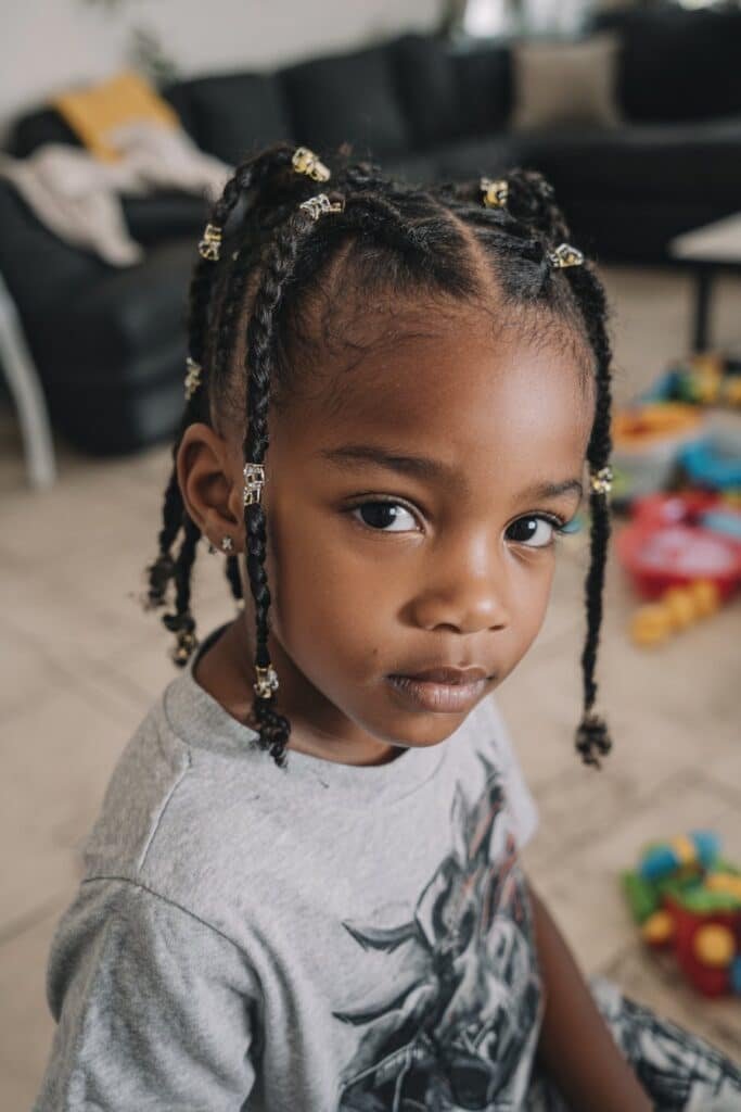A toddler girl with triangular part braids decorated with colorful beads, shot in a playful playroom environment.