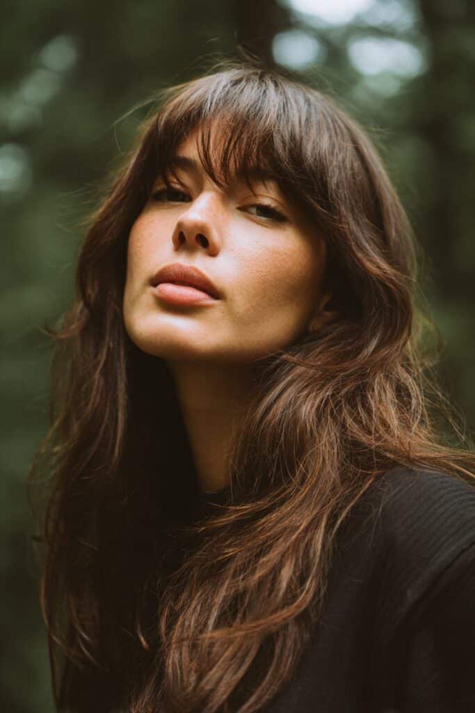 Woman with layered long hair and soft side part bangs showing volume and texture.