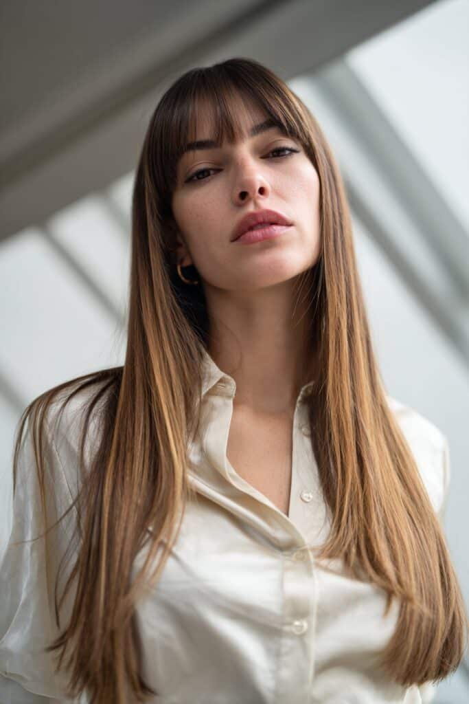 Young woman with sleek straight hair and polished side-part curtain bangs.