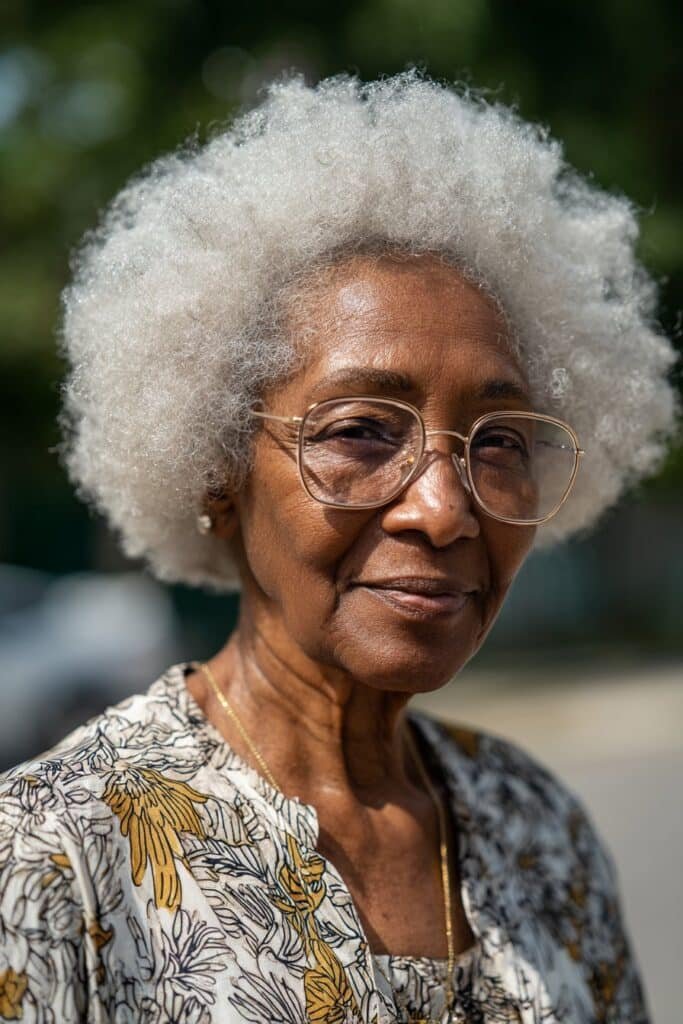 Older woman with glasses wearing a voluminous white afro hairstyle.